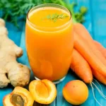 A cup of carrot caribbean smoothie with some ginger beside the cup.
