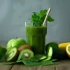 A cup of green healthy drink with some kiwi fruit and oregons.