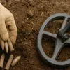 A man with glove is finding old bullets by metal detector.
