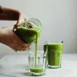 A green drink is hold by a hand pouring into a cup.