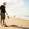 A man is man is using a metal detector to do a beach detecting.